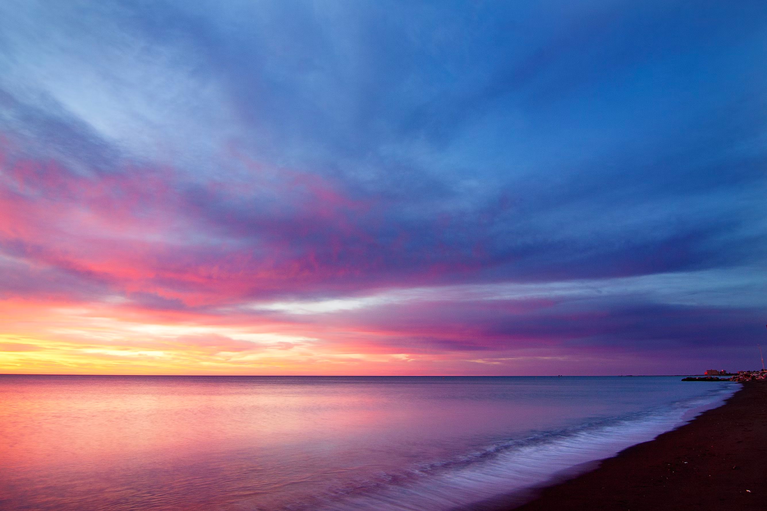 Coastal sunset photo with cotton candy colored clouds and very tame waves on the shore